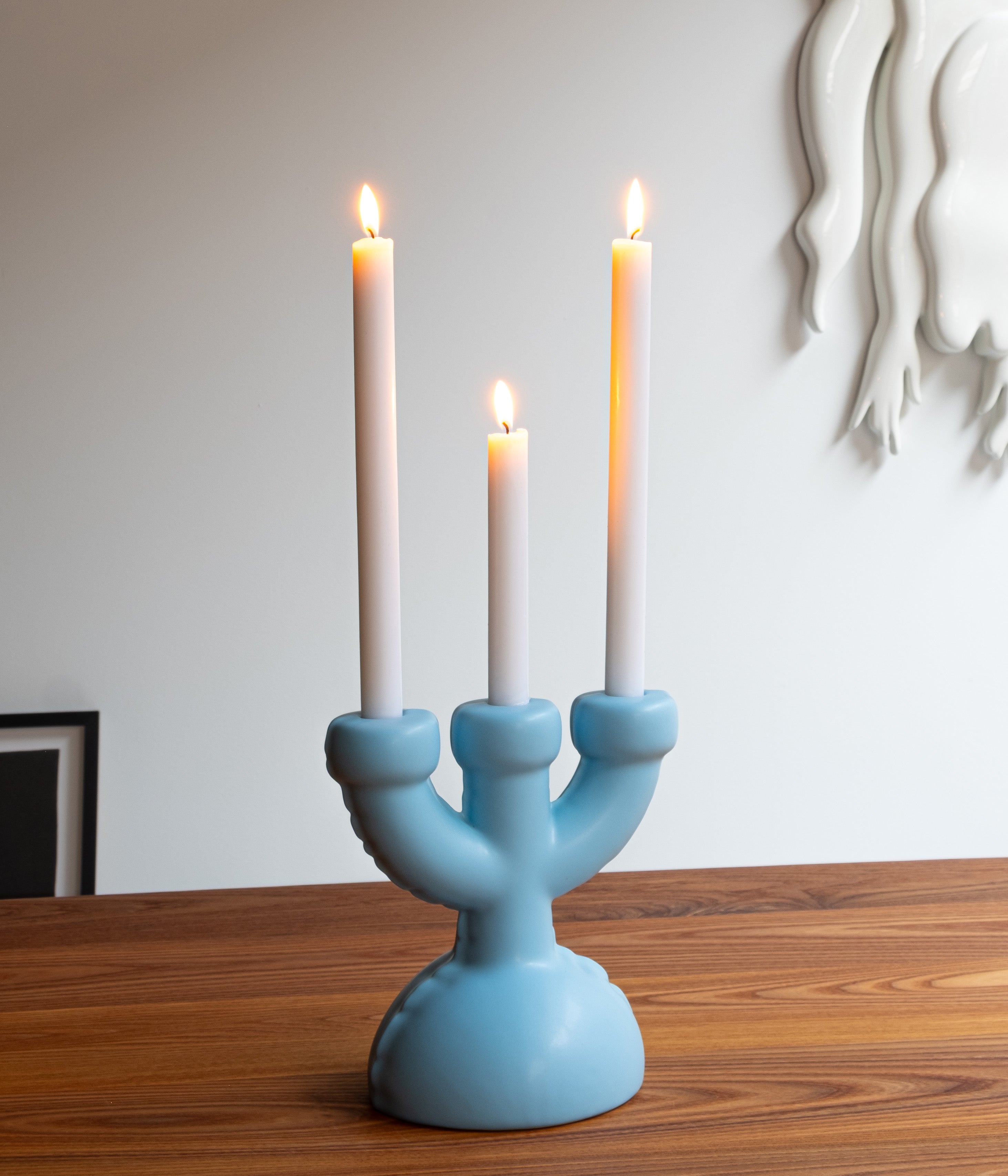 A blue Home Studyo ceramic design candelabra with a three-armed design, on a wooden table